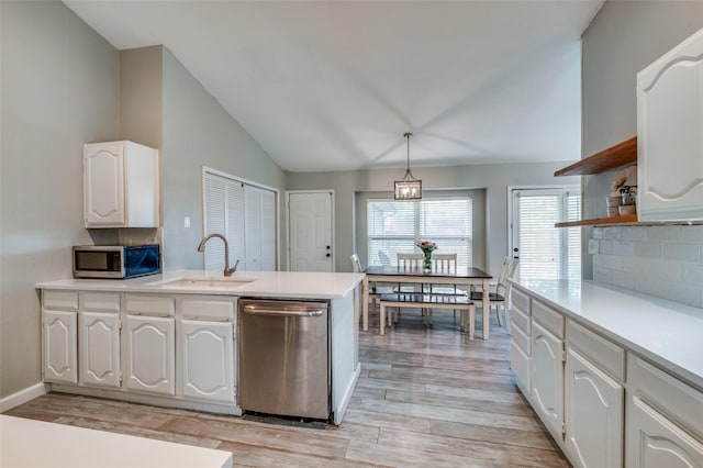 kitchen featuring a peninsula, white cabinetry, a sink, vaulted ceiling, and stainless steel appliances