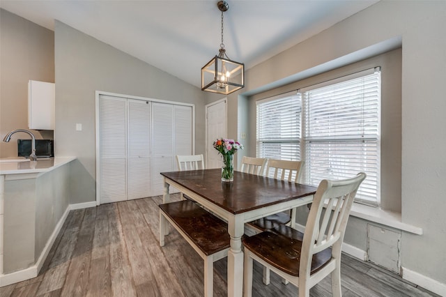 dining room with baseboards, a notable chandelier, light wood-style flooring, and lofted ceiling