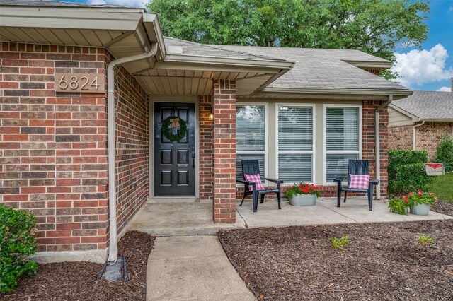 entrance to property with brick siding and a shingled roof
