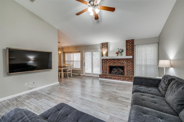living area featuring a brick fireplace, wood finished floors, lofted ceiling, baseboards, and ceiling fan with notable chandelier