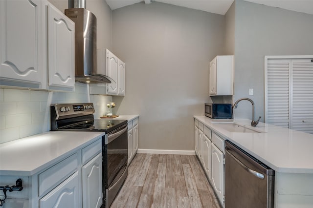 kitchen featuring appliances with stainless steel finishes, a sink, wall chimney exhaust hood, a peninsula, and light wood-type flooring