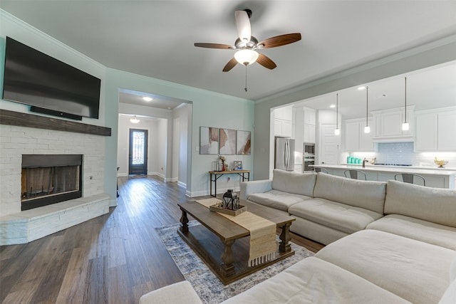 living room featuring crown molding, a fireplace, baseboards, ceiling fan, and dark wood finished floors