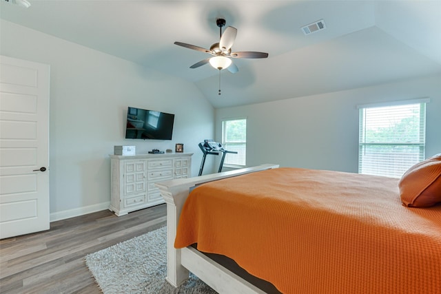 bedroom with a ceiling fan, visible vents, vaulted ceiling, wood finished floors, and baseboards