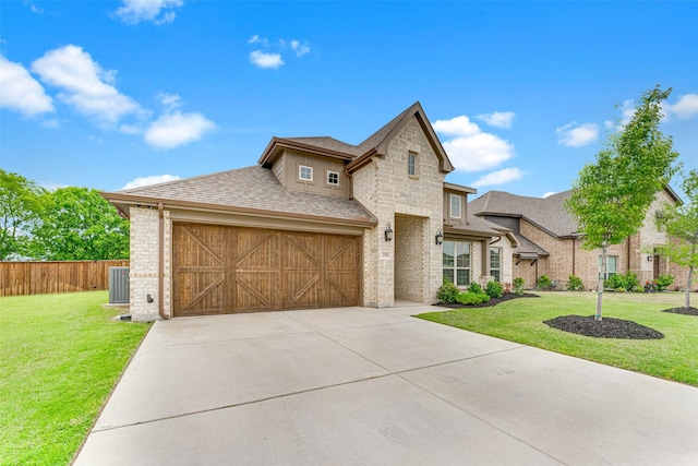 french country style house featuring roof with shingles, central AC unit, fence, a front lawn, and concrete driveway