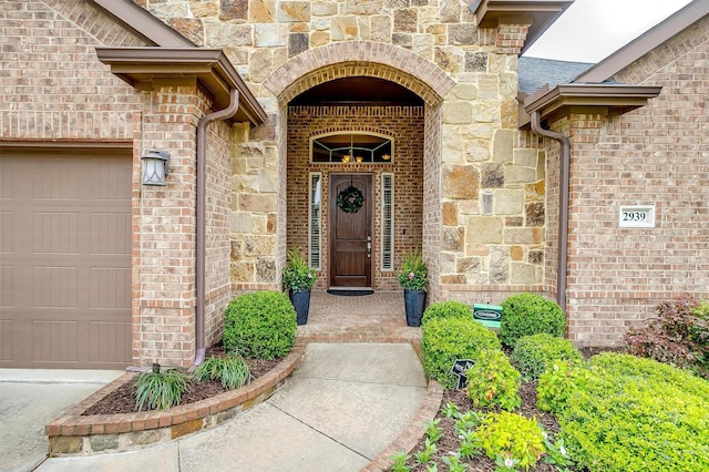 view of exterior entry featuring brick siding, a garage, and stone siding