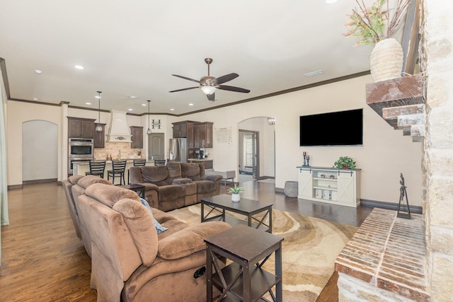 living area featuring a ceiling fan, dark wood-type flooring, baseboards, arched walkways, and ornamental molding