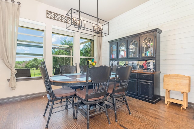dining space featuring baseboards, a notable chandelier, wooden walls, and wood finished floors