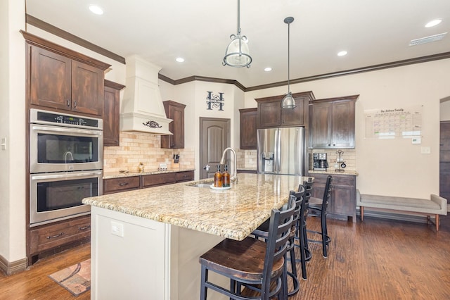 kitchen with premium range hood, dark wood-style flooring, light stone countertops, dark brown cabinets, and appliances with stainless steel finishes