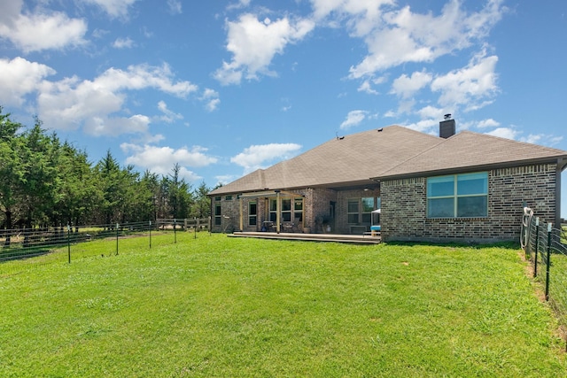 rear view of property featuring a chimney, fence, a lawn, brick siding, and a patio area