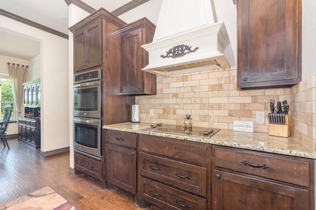 kitchen with stainless steel double oven, premium range hood, light stone counters, black electric stovetop, and dark wood-style floors