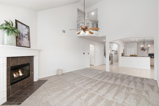 unfurnished living room with visible vents, arched walkways, a tile fireplace, carpet flooring, and ceiling fan with notable chandelier