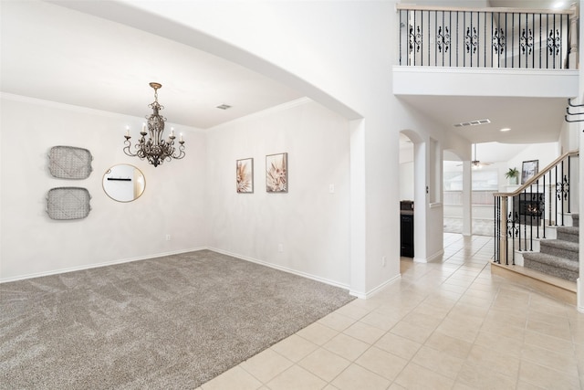 carpeted spare room featuring visible vents, ornamental molding, stairs, baseboards, and arched walkways