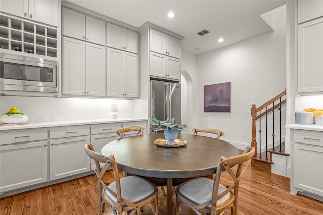 dining area with light wood-style floors, arched walkways, stairs, and visible vents