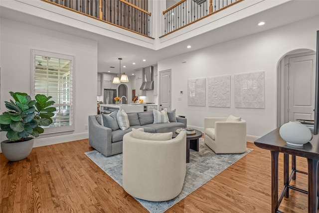 living room with arched walkways, light wood-style floors, baseboards, and a towering ceiling