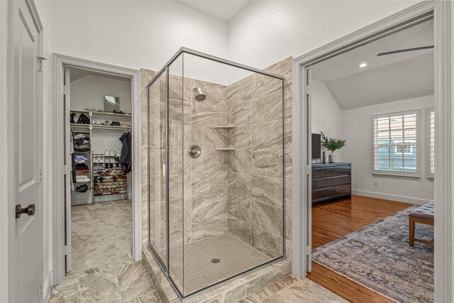 bathroom with baseboards, vaulted ceiling, a walk in closet, and a stall shower
