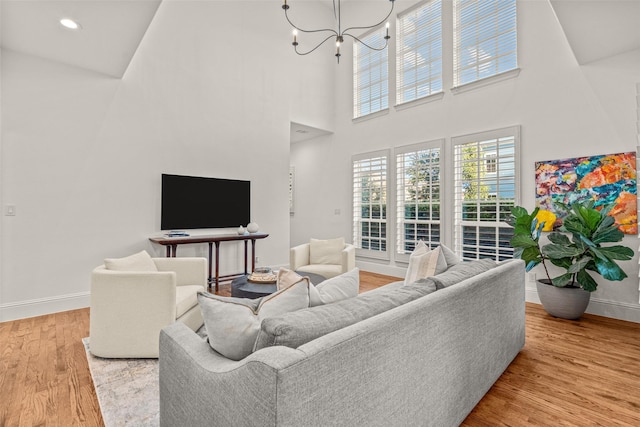 living room with an inviting chandelier, baseboards, a towering ceiling, and wood finished floors