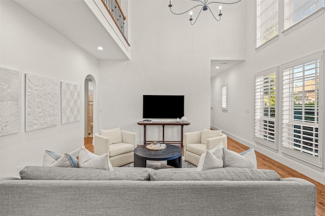 living room featuring arched walkways, a towering ceiling, wood finished floors, and a chandelier