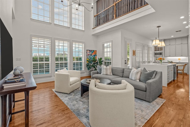 living area with light wood-style floors, recessed lighting, baseboards, a towering ceiling, and visible vents
