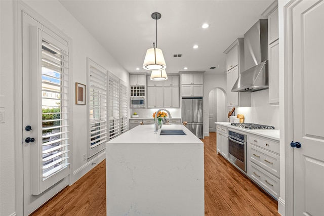 kitchen with appliances with stainless steel finishes, arched walkways, a sink, light countertops, and wall chimney exhaust hood
