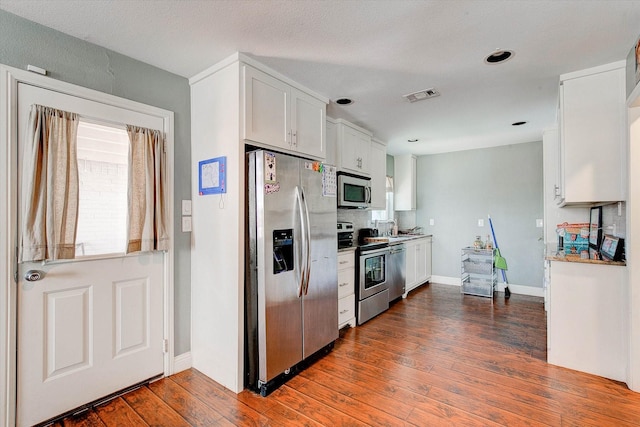 kitchen with white cabinets, dark wood-style flooring, appliances with stainless steel finishes, baseboards, and visible vents