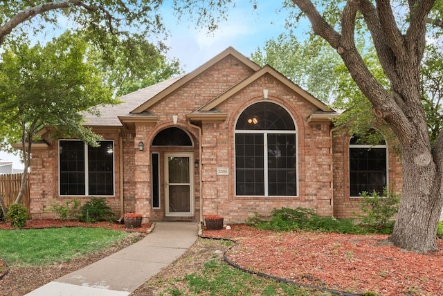 ranch-style home with brick siding, a shingled roof, a front lawn, and fence
