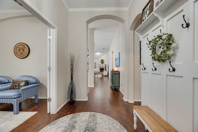 foyer with dark wood-style flooring, a fireplace, arched walkways, baseboards, and ornamental molding
