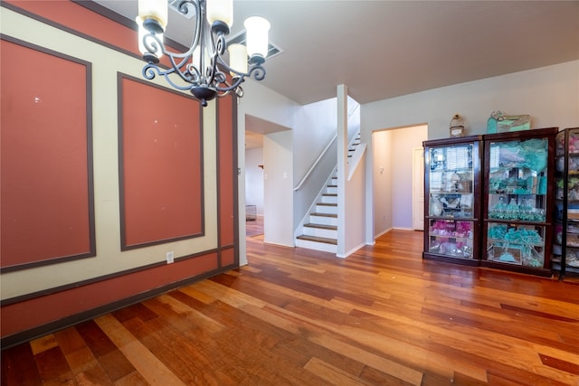 unfurnished dining area featuring baseboards, a notable chandelier, hardwood / wood-style floors, and stairway