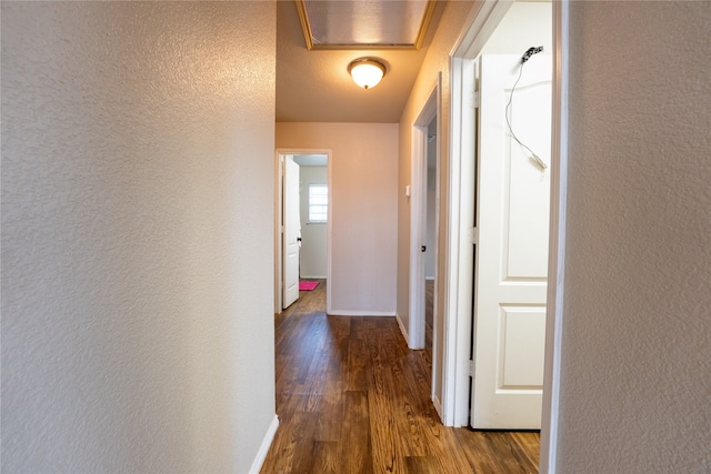 hall featuring baseboards, a textured wall, and dark wood finished floors
