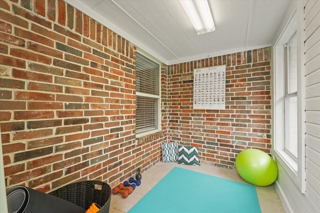 exercise room featuring tile patterned flooring and brick wall