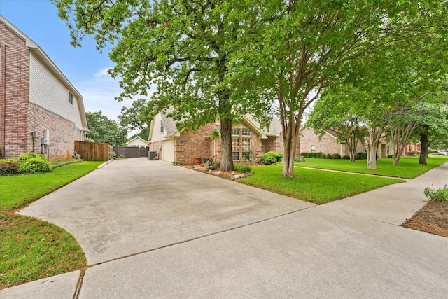 view of front facade featuring brick siding, fence, a front yard, and concrete driveway