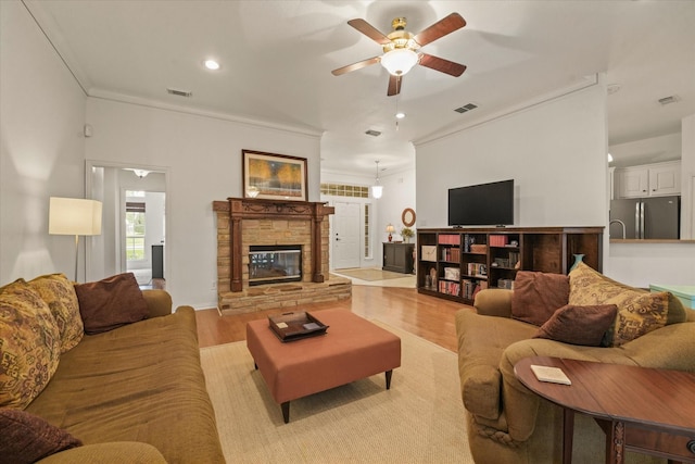 living area with crown molding, ceiling fan, light wood finished floors, and visible vents