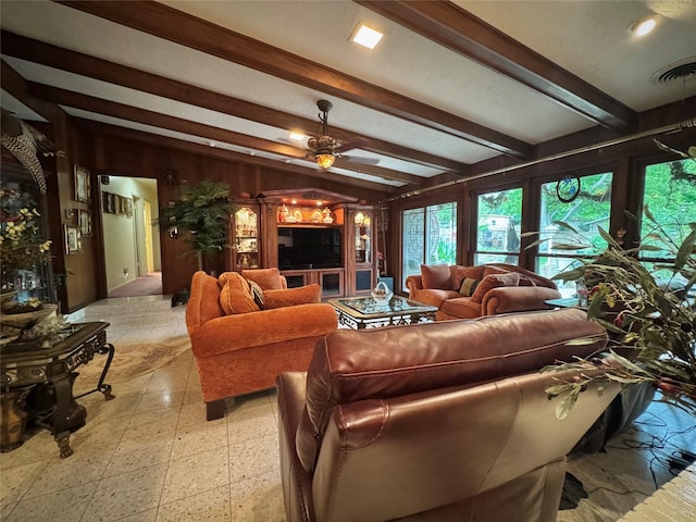 living area with wooden walls, beamed ceiling, a ceiling fan, and visible vents
