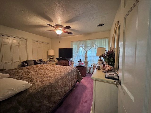 bedroom featuring visible vents, multiple closets, dark colored carpet, a textured ceiling, and a ceiling fan