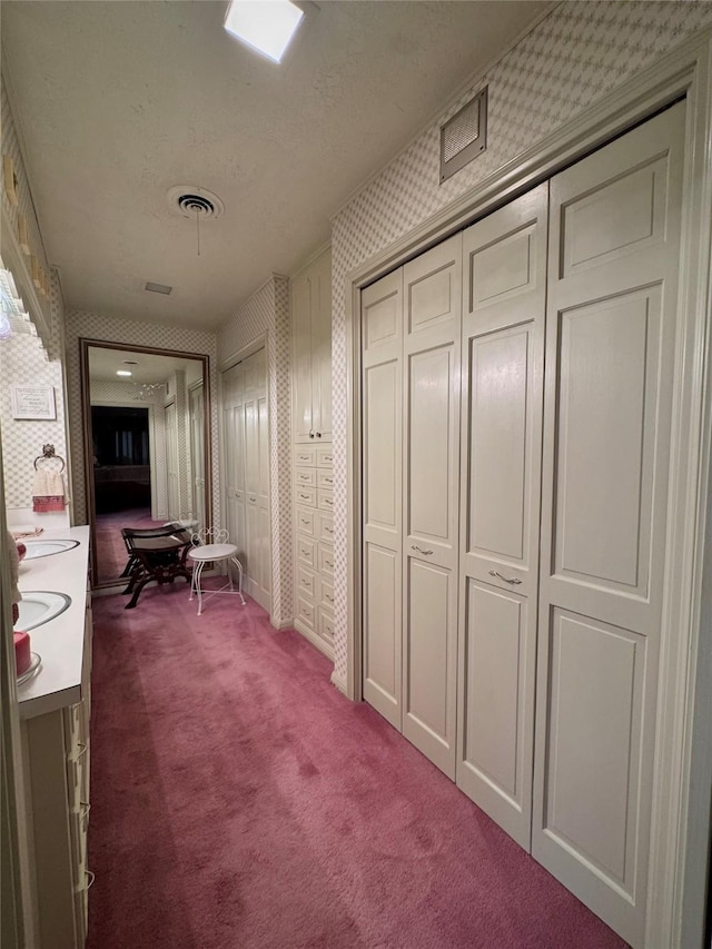 hallway featuring carpet floors, wallpapered walls, a textured ceiling, and visible vents