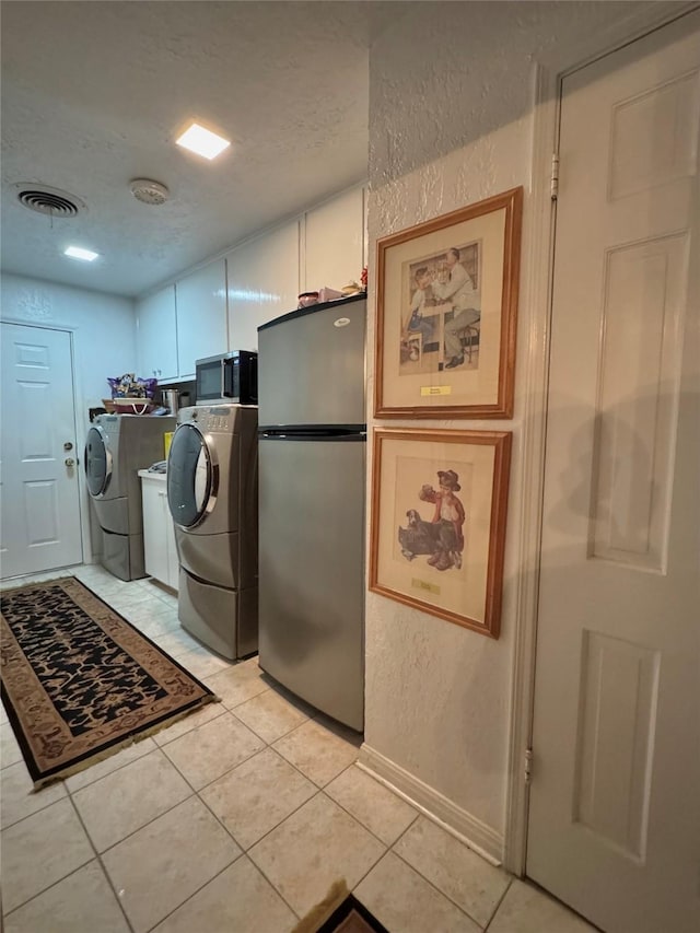 laundry area with visible vents, a textured wall, light tile patterned flooring, washing machine and clothes dryer, and cabinet space