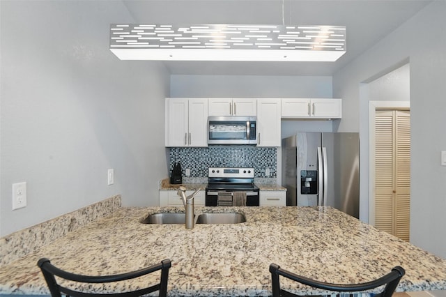 1933 Shaw St, Dallas, TX 75212 - kitchen featuring light stone counters, a sink, a kitchen breakfast bar, stainless steel appliances, and white cabinetry
