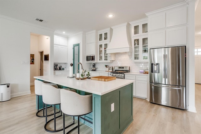 kitchen with appliances with stainless steel finishes, custom exhaust hood, light wood-style flooring, and visible vents
