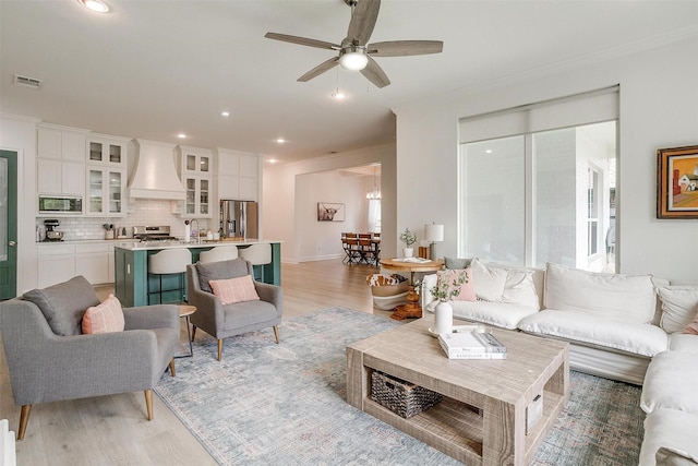 living room featuring ceiling fan, visible vents, ornamental molding, and light wood-style floors