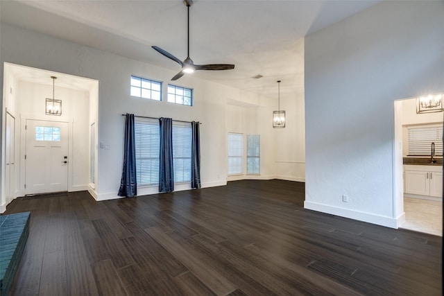 unfurnished living room with a towering ceiling, baseboards, dark wood-type flooring, a sink, and ceiling fan with notable chandelier