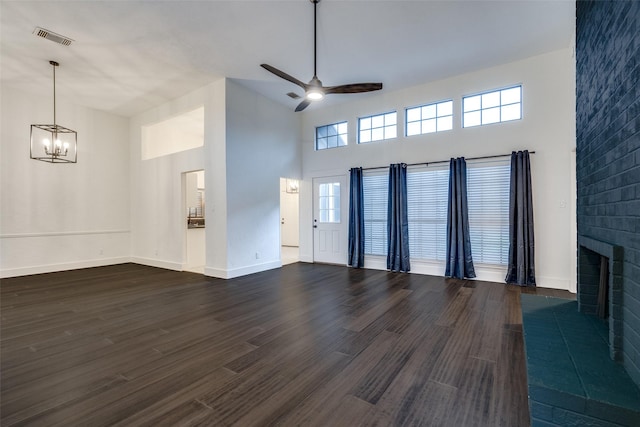 unfurnished living room with a high ceiling, dark wood finished floors, ceiling fan with notable chandelier, baseboards, and visible vents