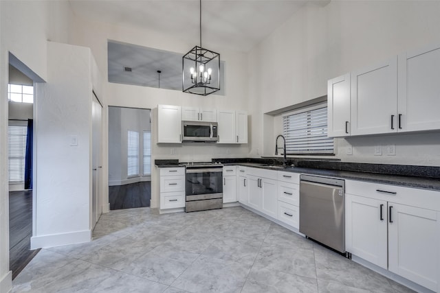 kitchen with a towering ceiling, appliances with stainless steel finishes, dark countertops, a sink, and an inviting chandelier