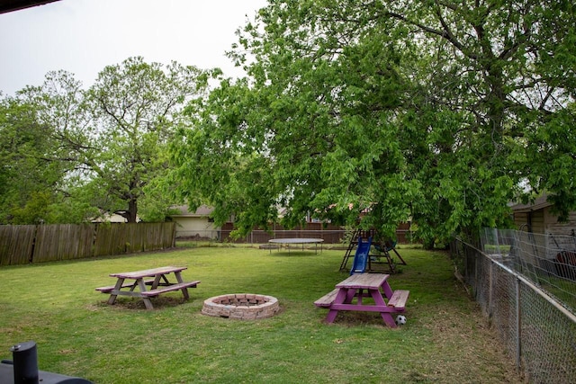 view of yard featuring a fire pit, a fenced backyard, and a trampoline