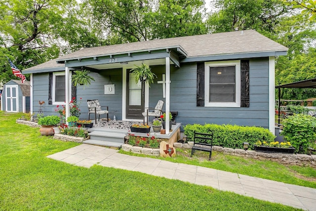 bungalow-style house with covered porch, a front yard, an outbuilding, a storage unit, and a shingled roof