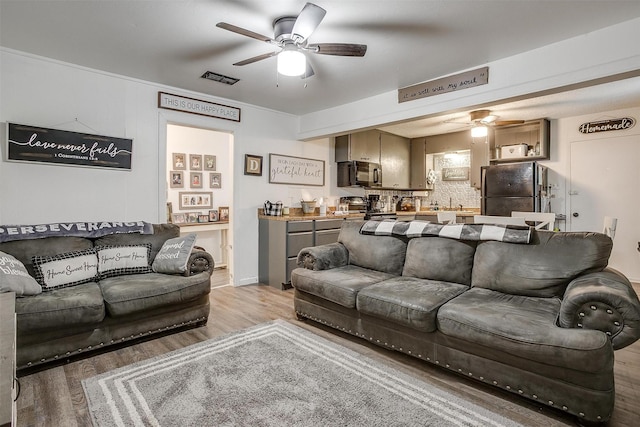 living room with light wood-style floors, a ceiling fan, and visible vents