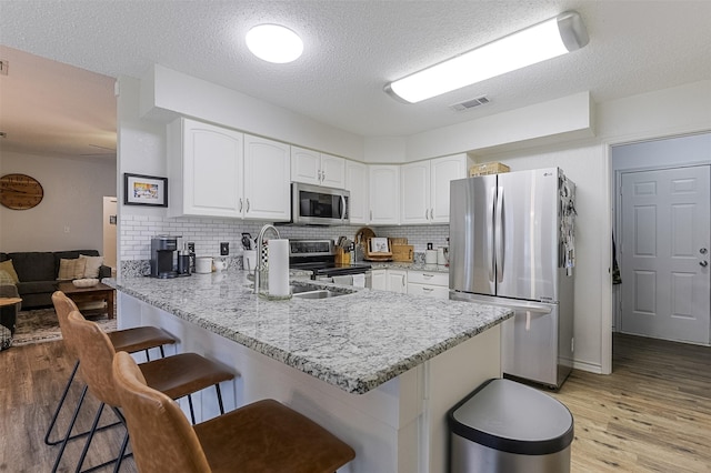 kitchen featuring visible vents, a peninsula, a kitchen bar, light wood-style flooring, and stainless steel appliances