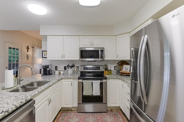 kitchen with a sink, appliances with stainless steel finishes, light stone counters, and white cabinetry