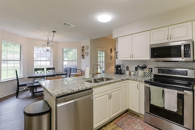 kitchen with visible vents, a peninsula, a textured ceiling, a sink, and appliances with stainless steel finishes