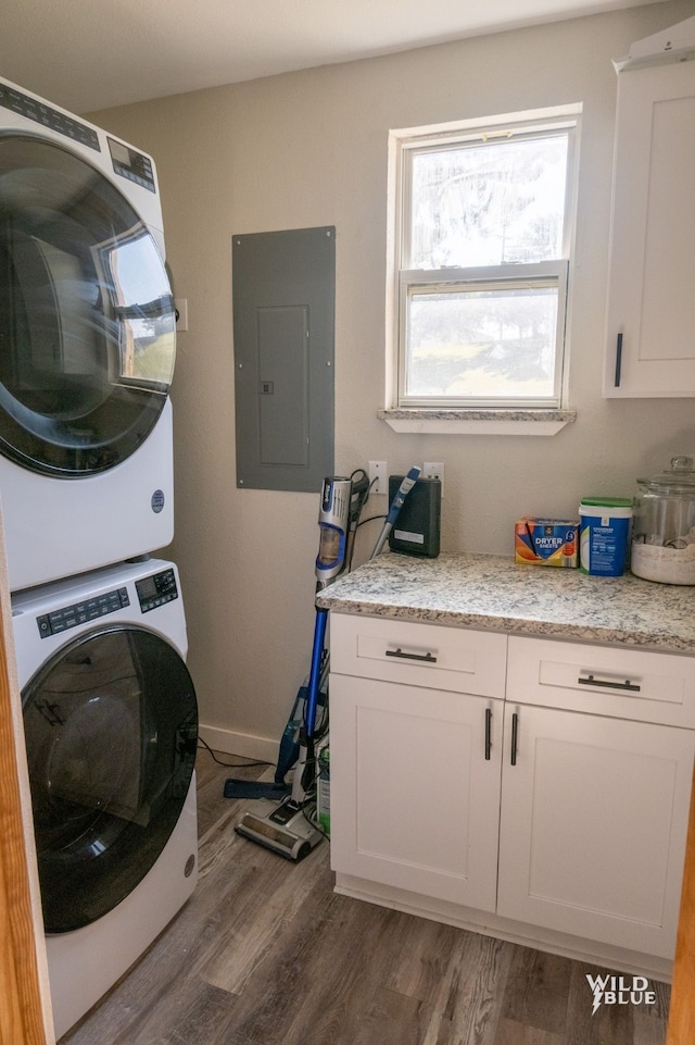 laundry area featuring cabinet space, stacked washer / drying machine, baseboards, wood finished floors, and electric panel