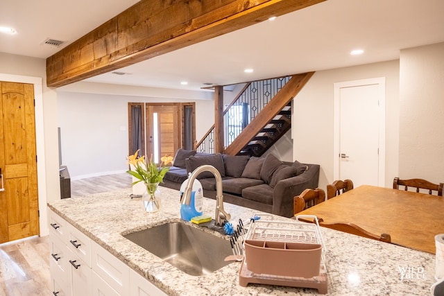 kitchen with white cabinets, light stone counters, a sink, light wood finished floors, and visible vents
