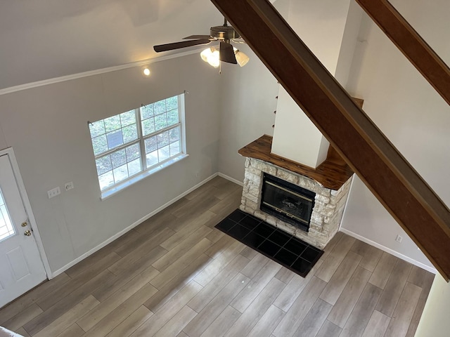 unfurnished living room featuring baseboards, a ceiling fan, wood finished floors, and a fireplace